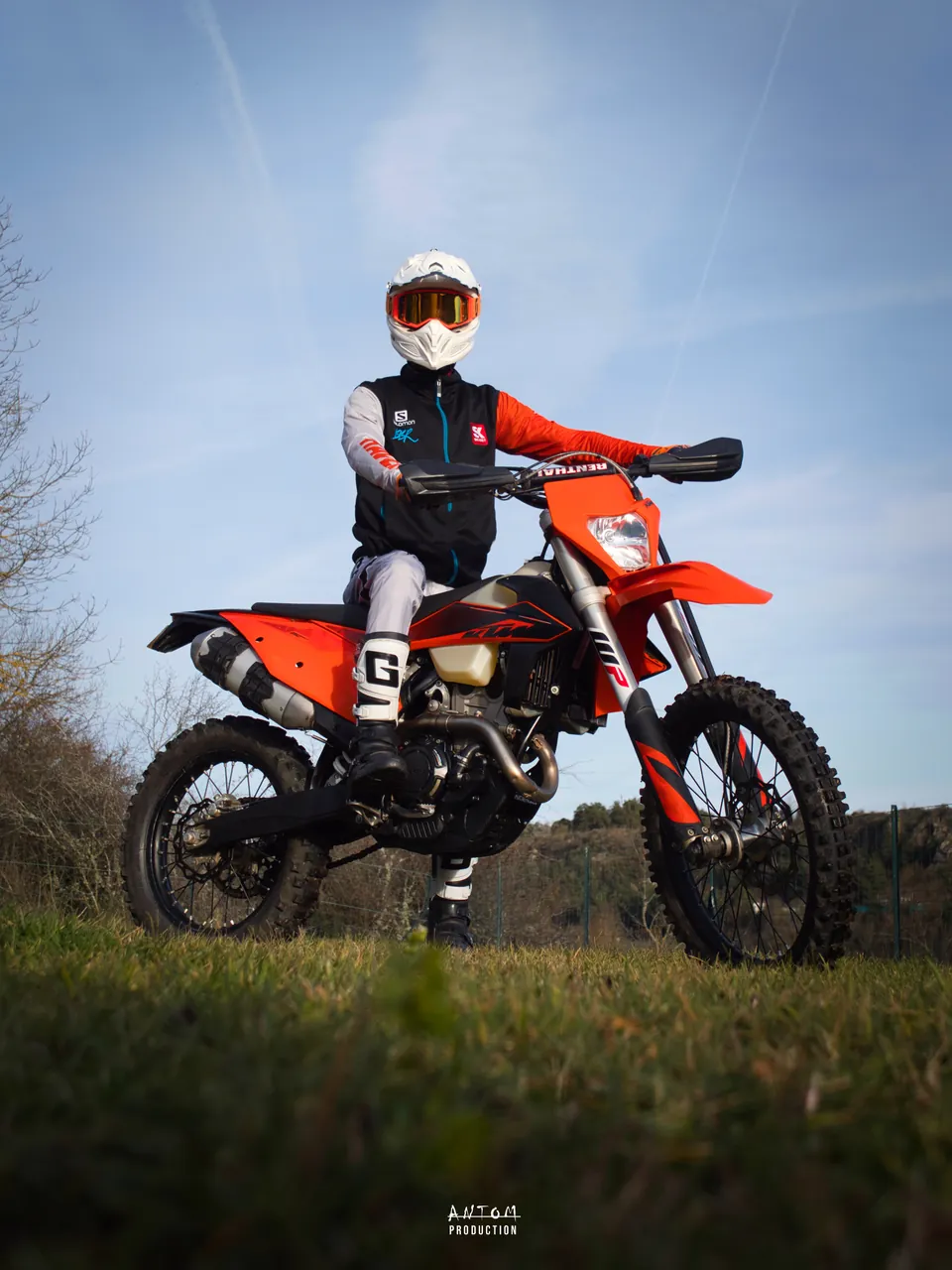 Portrait d'un pilote en tenue sur sa moto d'enduro orange, en contre-plongée